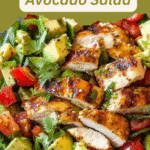 Colorful bowl of grilled chicken avocado salad with cherry tomatoes, cilantro, and lime dressing on a rustic table